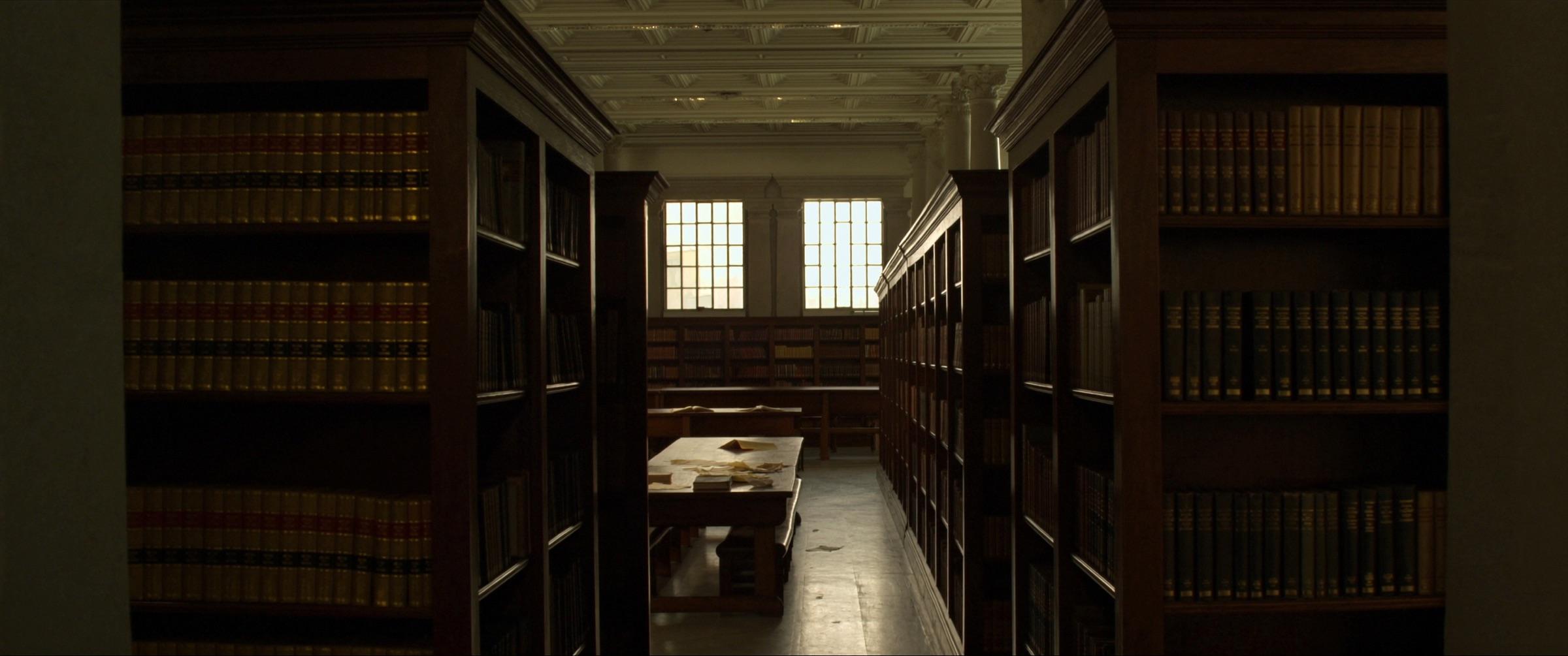 Salle de lecture d'une bibliothèque de droit : rayonnages de volumes reliés, table de travail, hautes fenêtres.