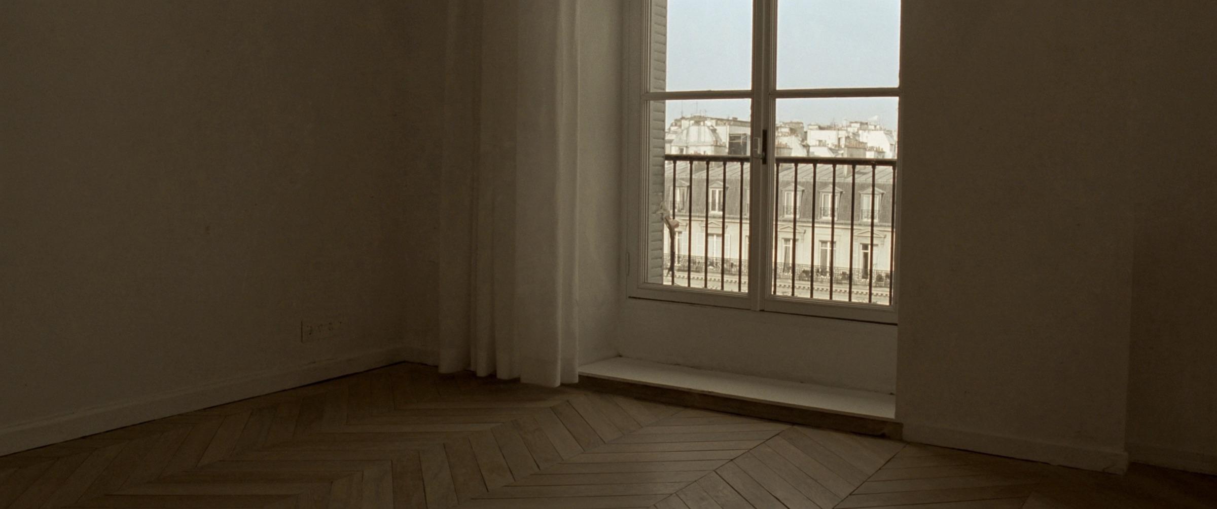 Un appartement vide et fini : parquet en point de Hongrie, murs blancs, hautes fenêtres ouvertes sur la ville.