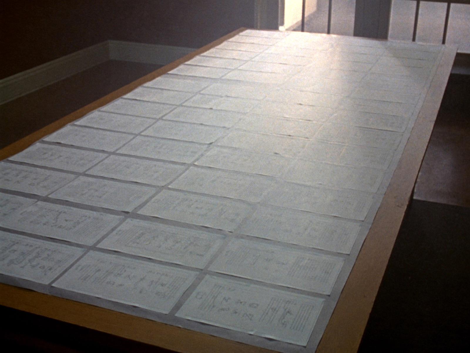 Des dizaines de documents disposés en grille sur une longue table en chêne.
